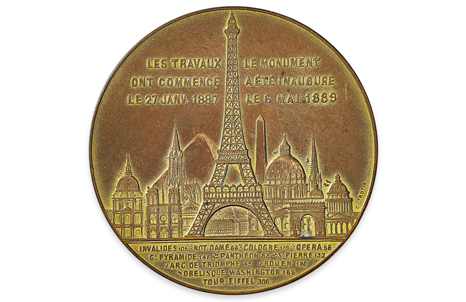 A bronze medal celebrating the Eiffel Tower’s completion in 1889, showing the tower surrounded by famous global landmarks with French inscriptions detailing its construction and inauguration dates