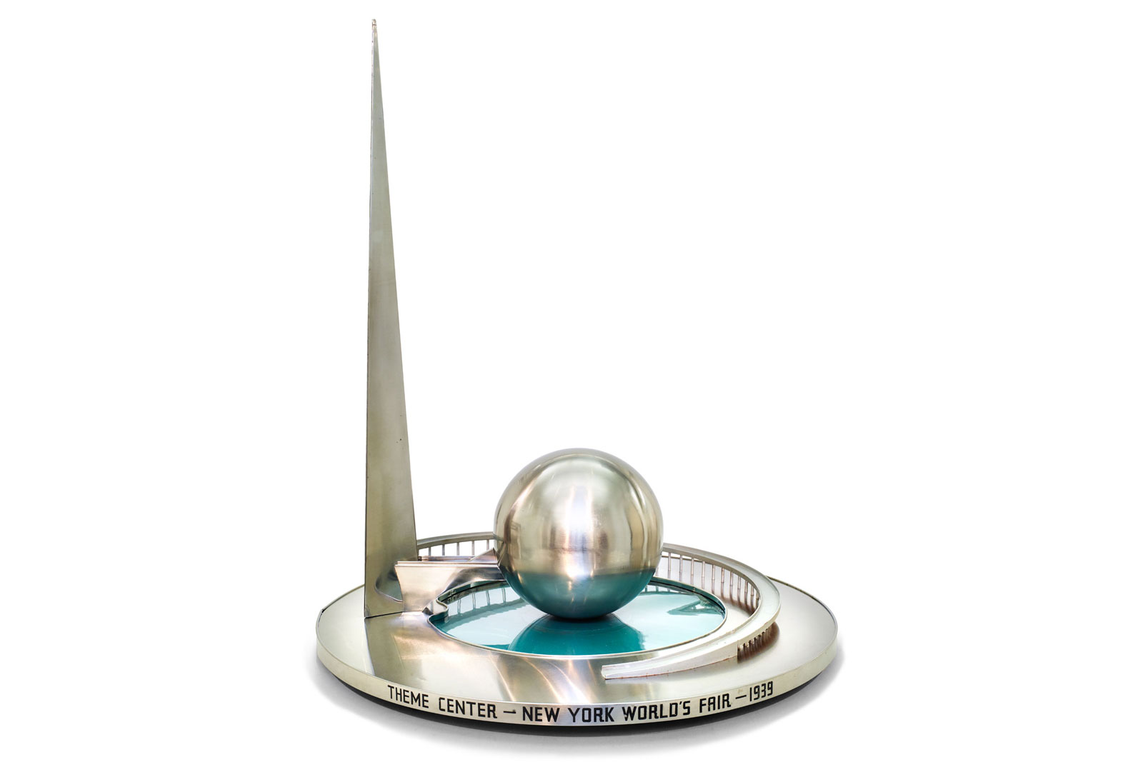 A sleek silver model of the 1939 New York World’s Fair theme center, showcasing the Trylon and Perisphere structures set on a circular platform with a futuristic, streamlined design