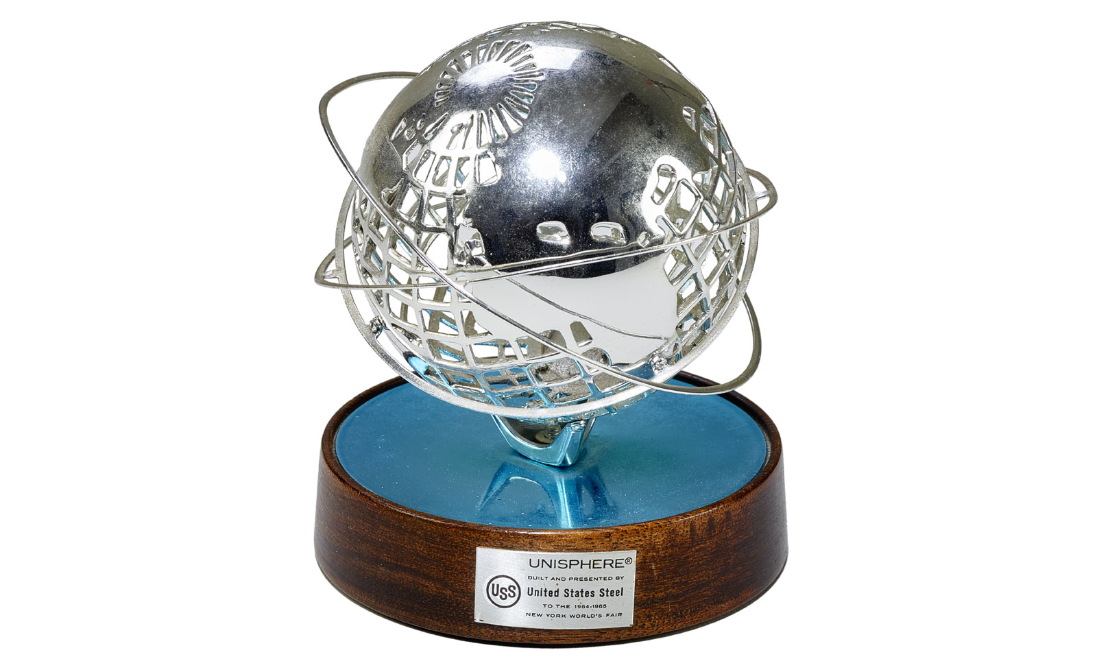 A small metallic sculpture of the Unisphere, a spherical globe with three orbit rings, mounted on a round wooden base with a metal plaque that reads: “UNISPHERE® built and presented by United States Steel to the 1964–1965 New York World's Fair”