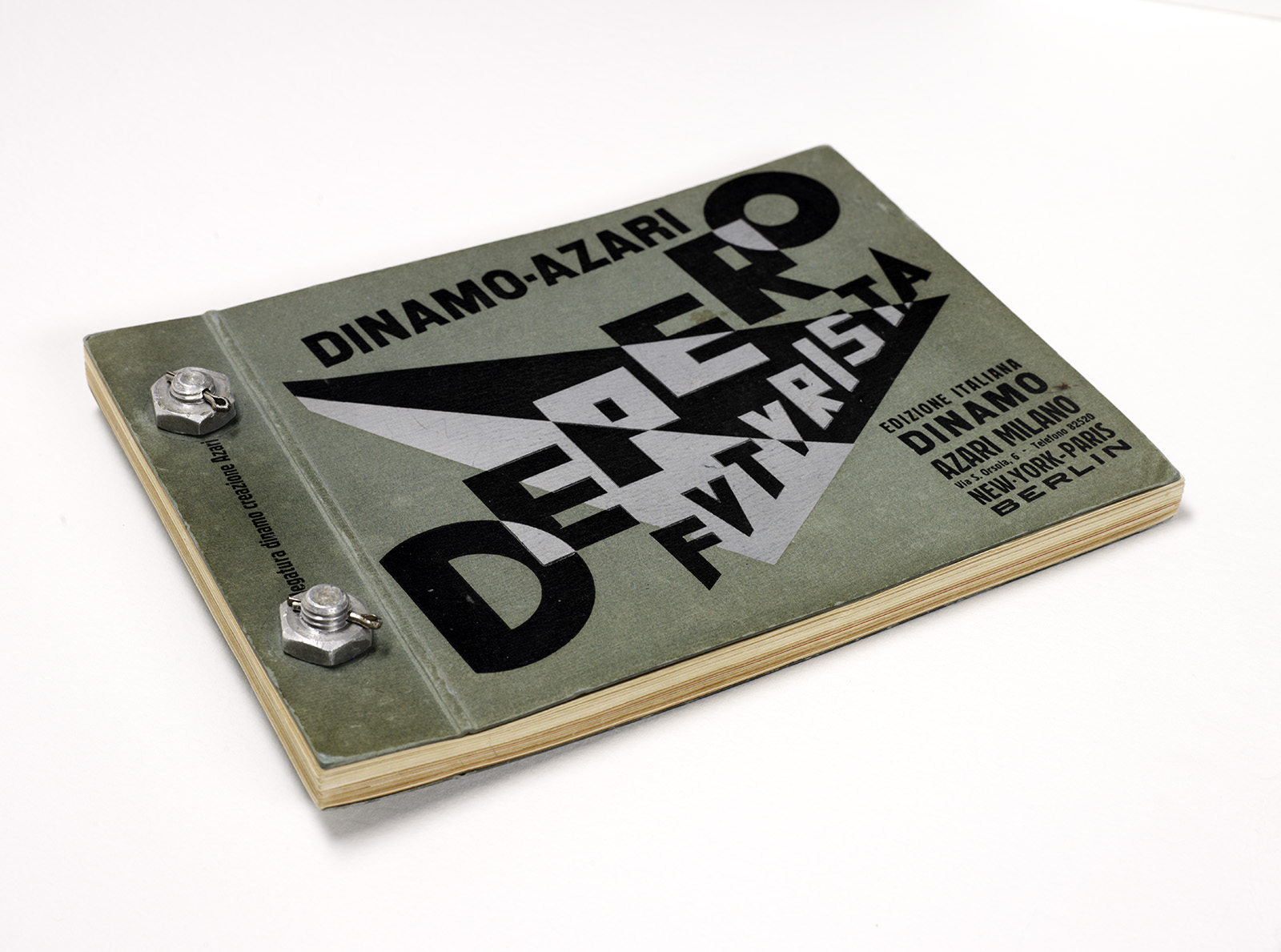 A green booklet titled Dinamo-Azari Depero Futurista with bold black text and graphics on the cover. It has metal bolt bindings and is slightly open, revealing multiple pages.