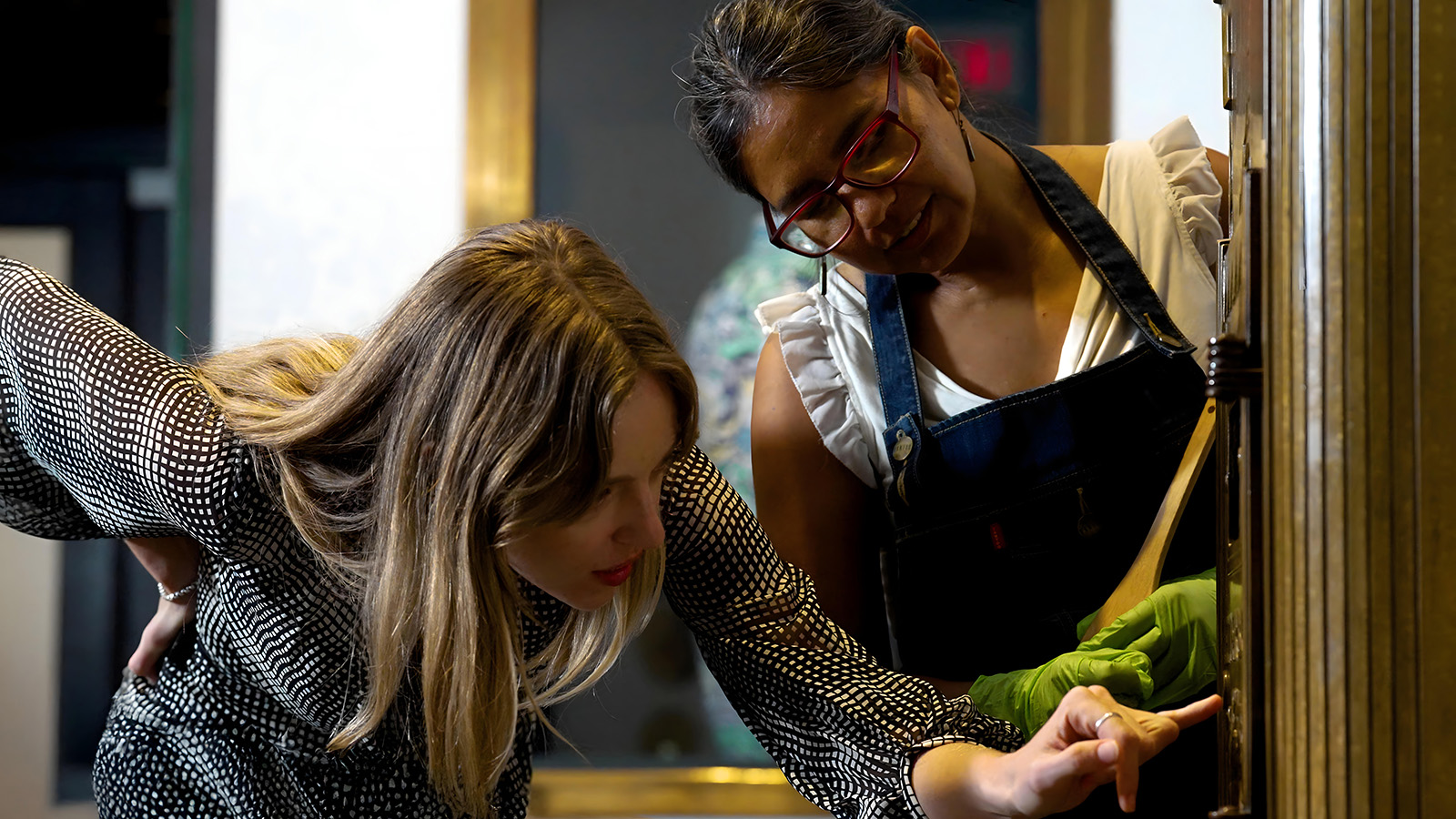 Art director Brittany Ballinger and assistant director of collections Silvia Manrique in The Wolfsonian lobby, examining a bronze mailbox.