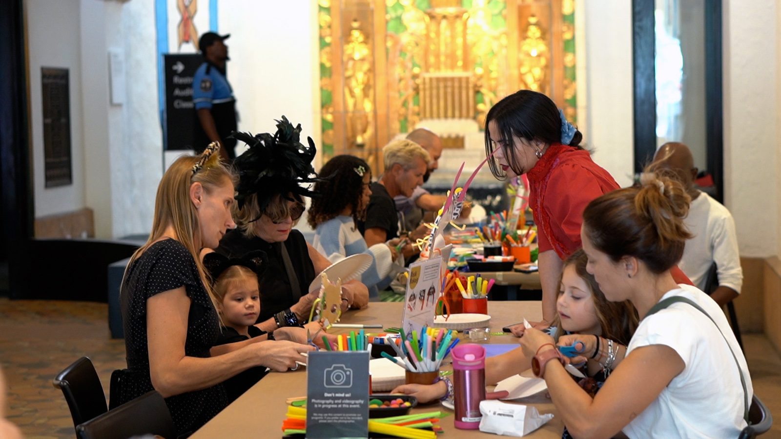 Families and children participate in a colorful craft activity at a long table during a museum event